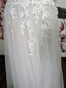 Ein Brautkleidrock aus feinem Tüll, verziert mit kunstvollen Spitzenapplikationen, die wie zarte Blütenranken herabfließen und eine romantische und traumhafte Optik erzeugen.