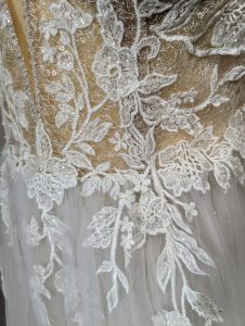 Nahaufnahme der detaillierten Spitzenarbeit mit eingearbeiteten Perlen auf einem Brautkleid, die einen tiefen Einblick in die feine Handwerkskunst und das elegante Design des Kleides gibt.