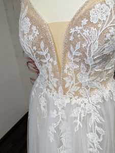 Detailreiche Ansicht des V-Ausschnitts eines Brautkleids, das mit kunstvoller Spitze besetzt ist und sanft in einen fließenden Tüllrock übergeht, was eine raffinierte und romantische Ästhetik vermittelt.