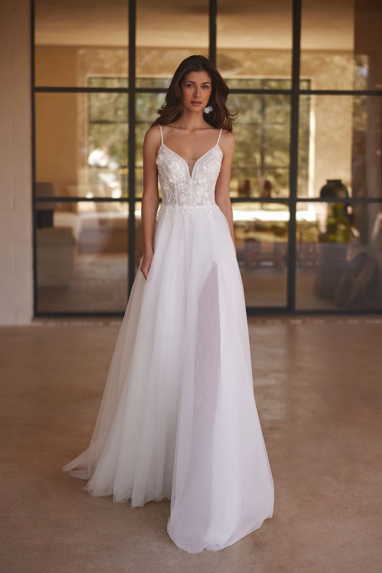 Elegantes Brautkleid in A-Linie mit tiefem V-Ausschnitt und floralen Spitzenapplikationen, fotografiert in einem modernen Raum.