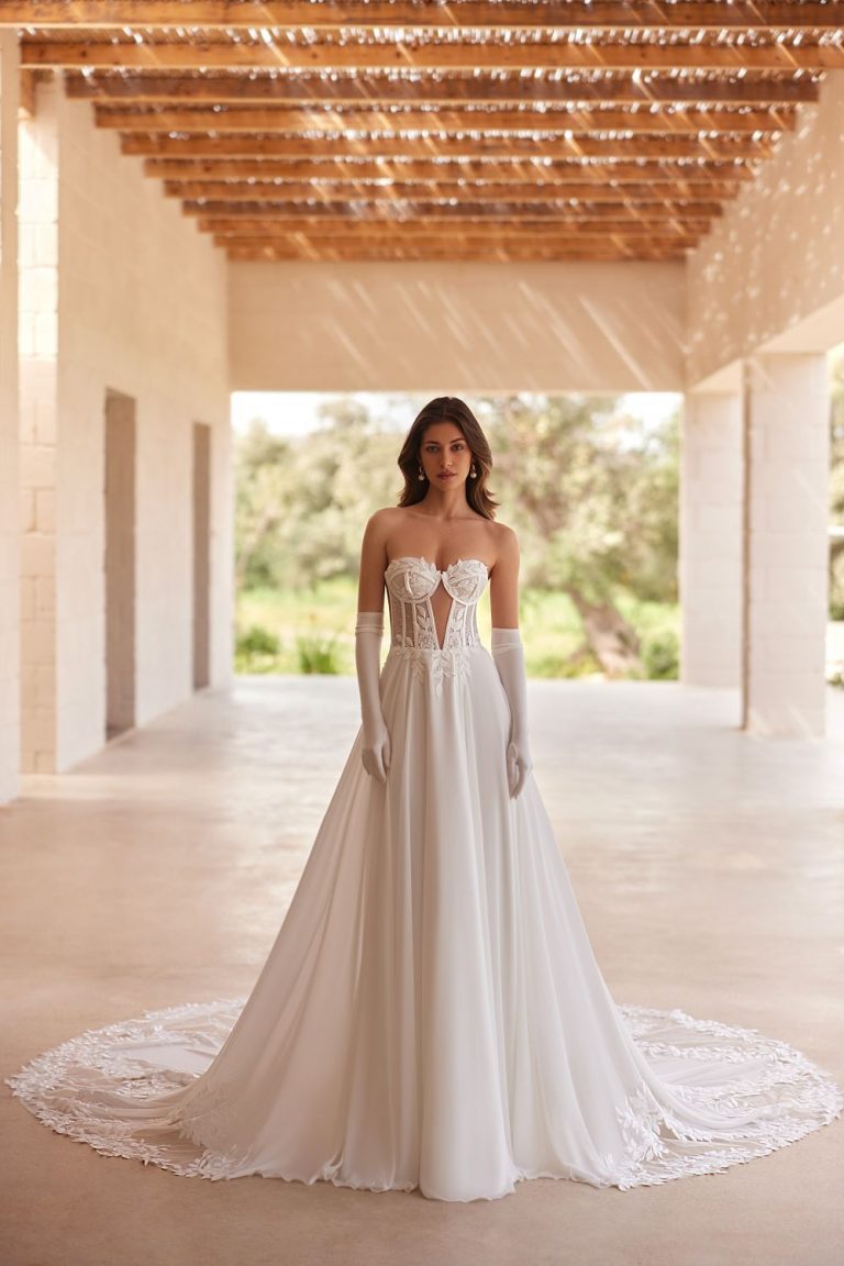 rägerloses Brautkleid mit Herz-Ausschnitt, floraler Spitze und fließendem Rock, aufgenommen in einem lichtdurchfluteten Innenhof.