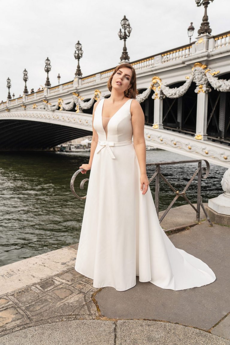 Brautkleid in A-Linie für kurvige Frauen mit tiefem V-Ausschnitt vor romantischer Brücke.