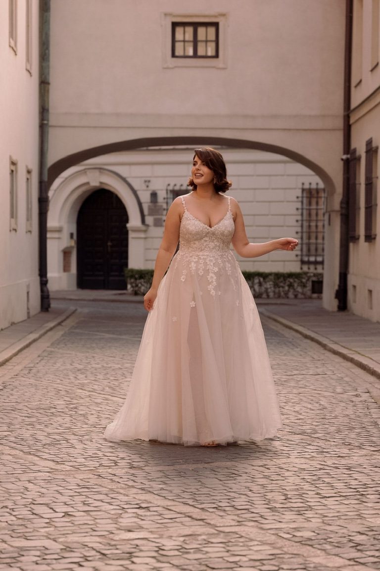 Braut in einem A-Linien-Brautkleid aus Tüll und Spitze mit 3D-Blumenapplikationen auf einer Kopfsteinpflasterstraße.