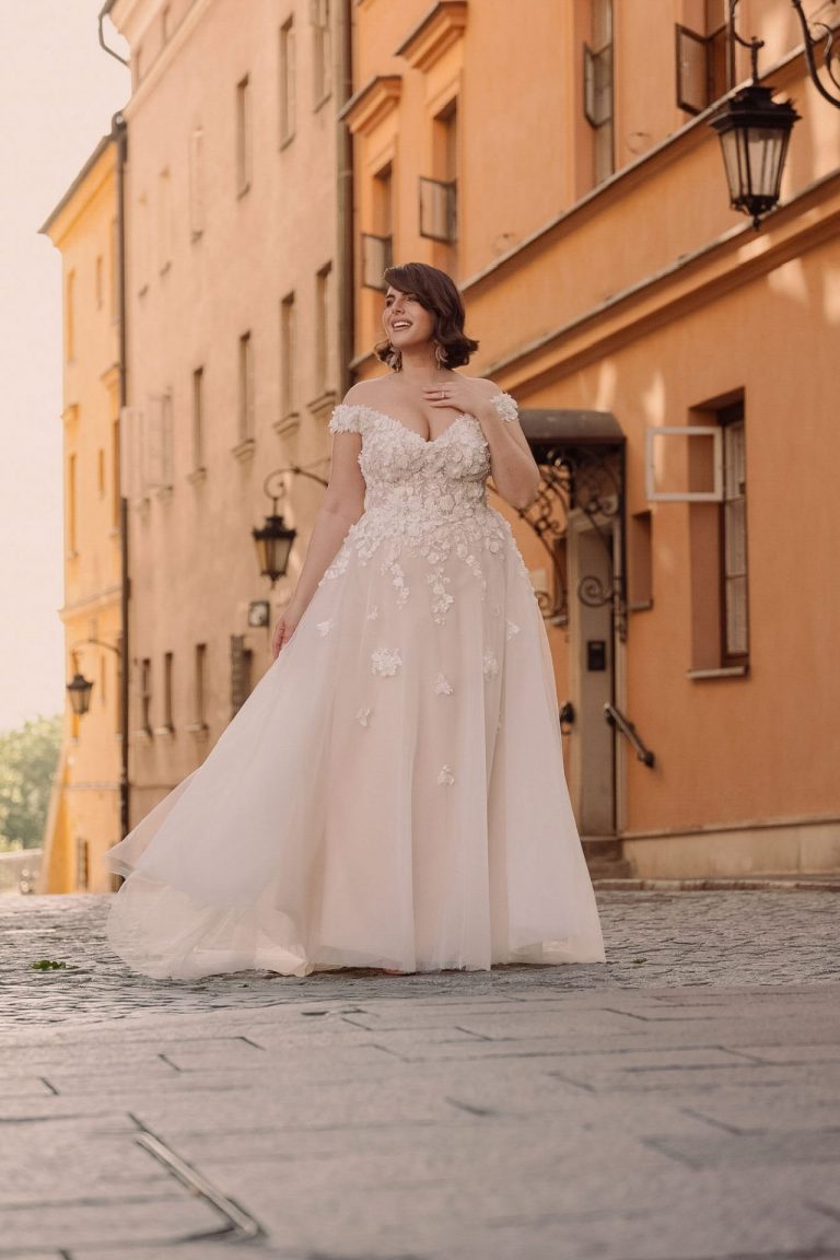 Curvy Braut in A-Linien-Brautkleid mit floralen Applikationen und Tüllrock in romantischer Altstadt.