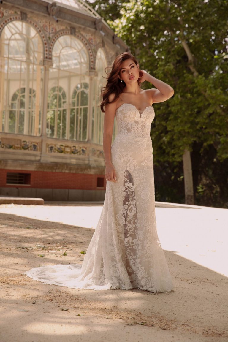Braut in einem Fit-and-Flare-Brautkleid mit floraler Spitze vor einem gläsernen Pavillon.