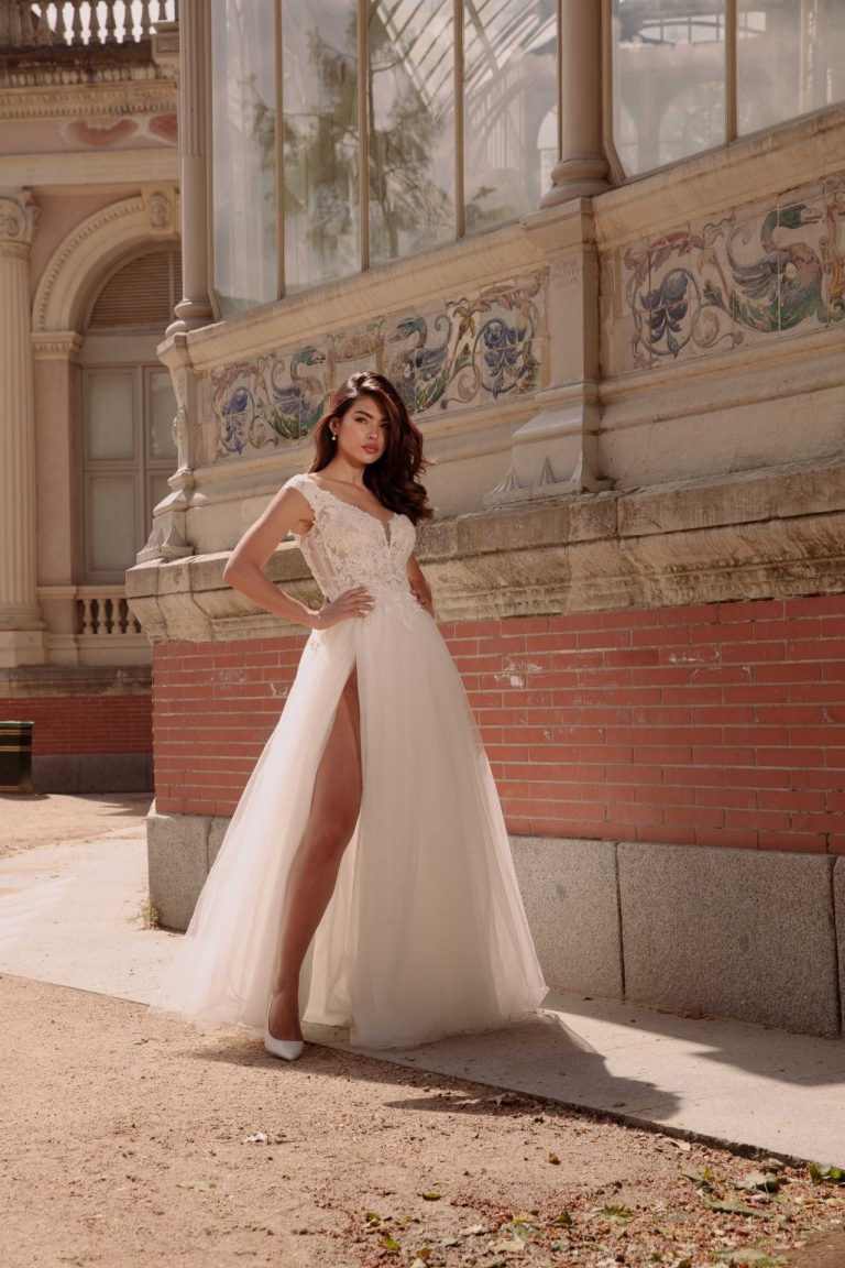 Brautkleid mit floraler Spitze, A-Linie und Schlitz im Tüllrock, aufgenommen vor einem eleganten Gebäude.