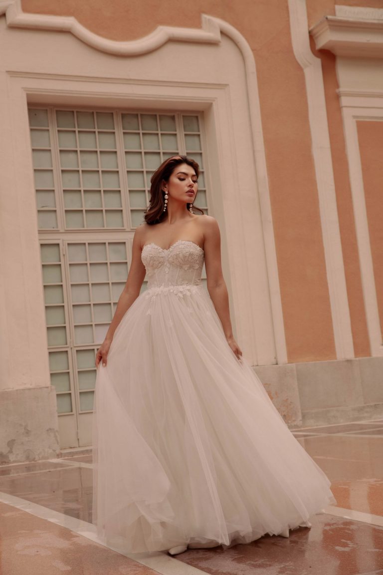 Brautkleid in A-Linie mit trägerlosem Korsett und Tüllrock vor einem eleganten Gebäude.