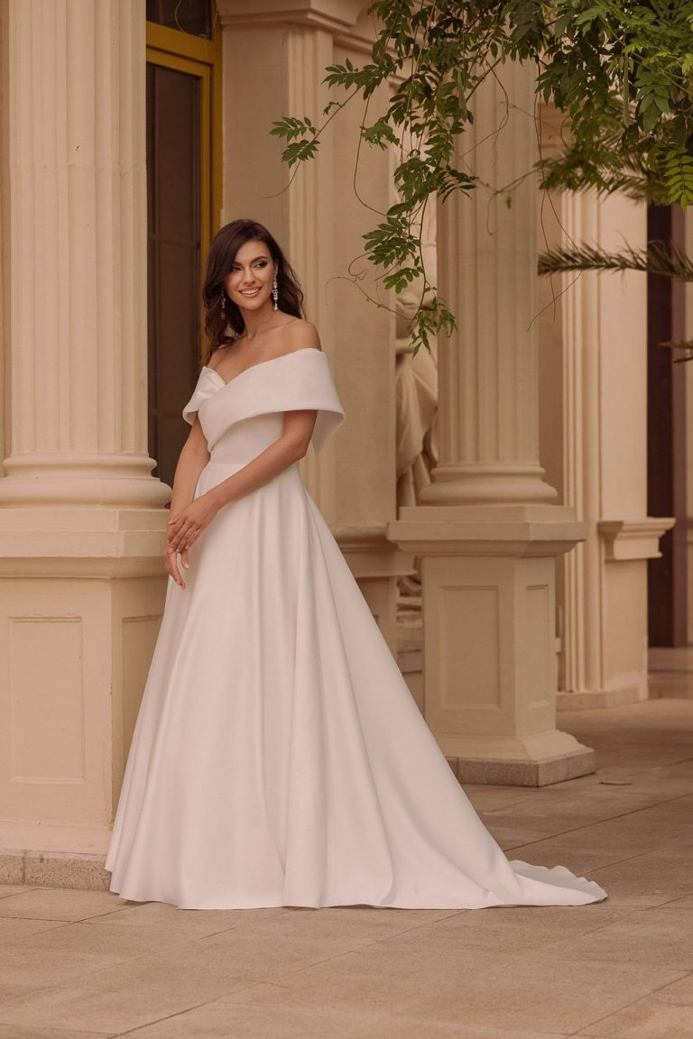 Brautkleid mit Off-Shoulder-Ausschnitt und A-Linien-Schnitt vor klassischer Architektur