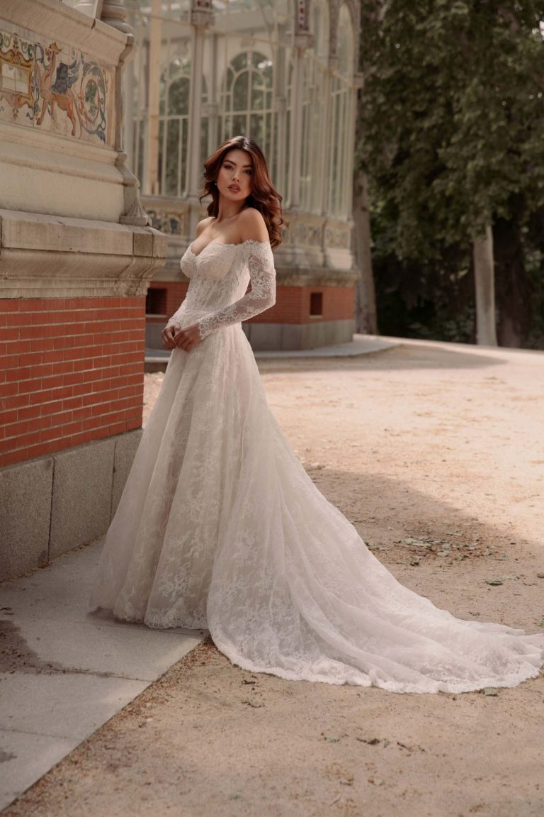Brautkleid mit Off-Shoulder-Design, langen Spitzenärmeln und fließendem Rock in einer romantischen Location.